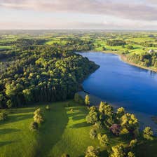 Aerial view of lush green landscapes and a clear blue lake at Castle Leslie Estate